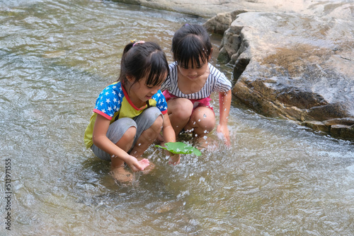 Happy cute little girl and her sister playing water in the stream. Little Asian sister enjoys swimming in the river. Healthy Summer Activities for Kids.