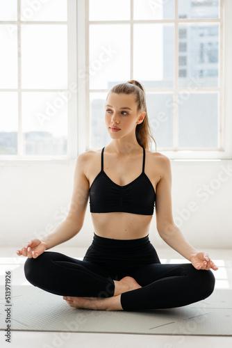 Sports girl meditating on a fitness mat against the background of a window