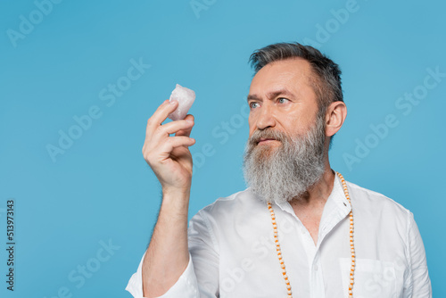 mastermind guru with grey beard looking at crystal of selenite isolated on blue. photo