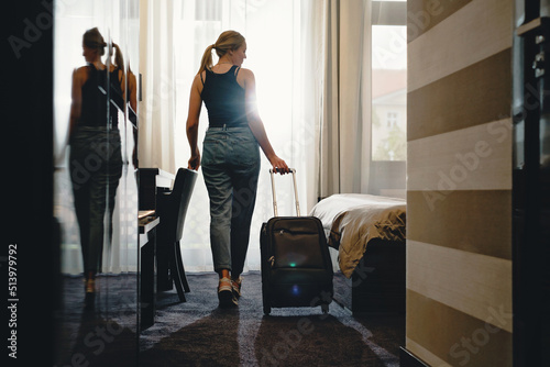 Woman traveler with luggage suitcase after checking Into a Hotel Room looking in the window. Silhouette of visitor in travel accommodation Person looking at bed, Sun flare from window 