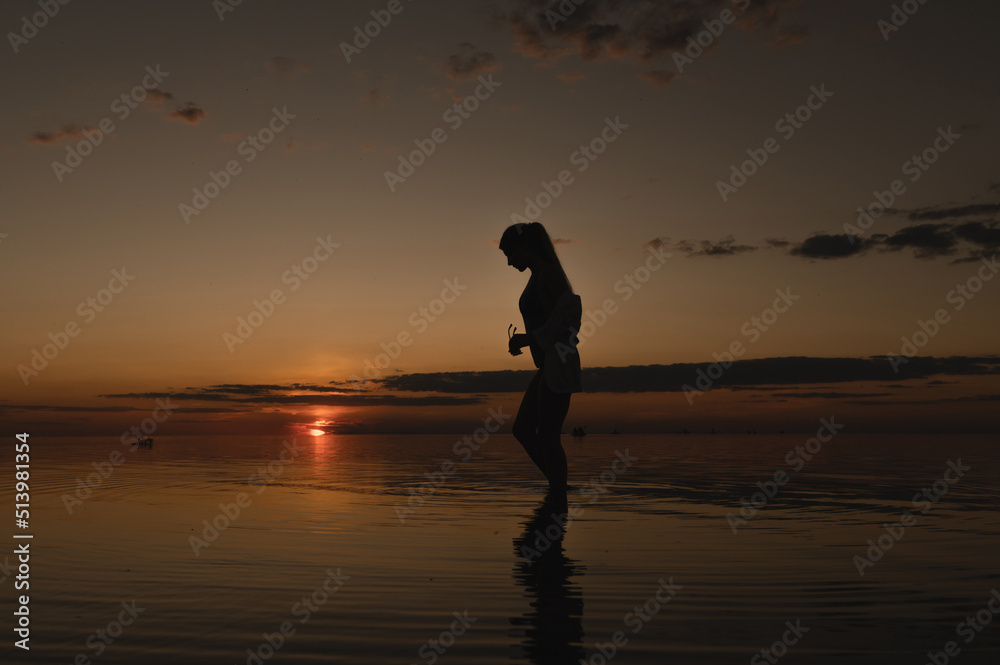 The girl is standing near the sea. The girl looks at the sunset on the sea