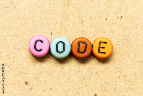 Round color bead with black letter in word code on wood background