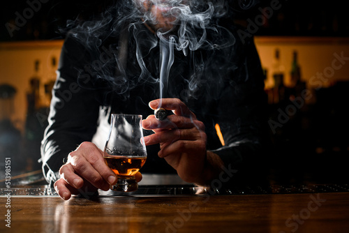 Gorgeous view of male hands holding a glass of alcoholic drink and smoking cigar photo
