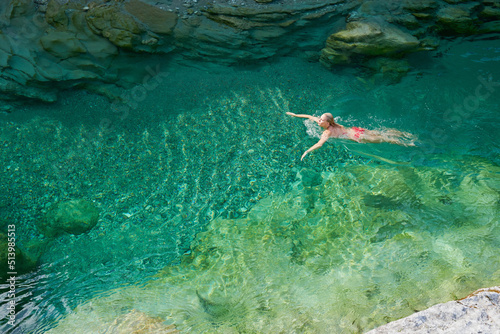 Overhead of a young woman on an adventure, swimming in an exotic blue river. Woman having fun relaxing in a lake on a travel vacation from above © Bevan G/peopleimages.com