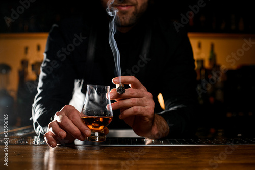 Great view of male hands holding a glass of alcoholic drink and smoking cigar photo