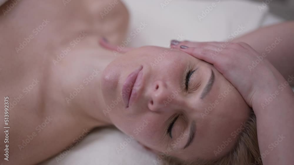Close-up headshot of satisfied client looking at camera talking enjoying neck massage in beauty spa. Beautiful blond Caucasian woman posing in slow motion as unrecognizable masseur doing procedure Close-up headshot of satisfied client looking at camera talking enjoying neck massage in beauty spa. Beautiful blond Caucasian woman posing in slow motion as unrecognizable masseur doing procedure