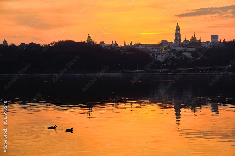 Kiev-Pechersk Lavra and city lights. Silhouette panorama at sunset of the colorful sky over the Dnieper river with passing ducks in Kyiv