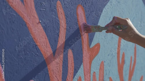 Person painting colourful mural on wall, close up