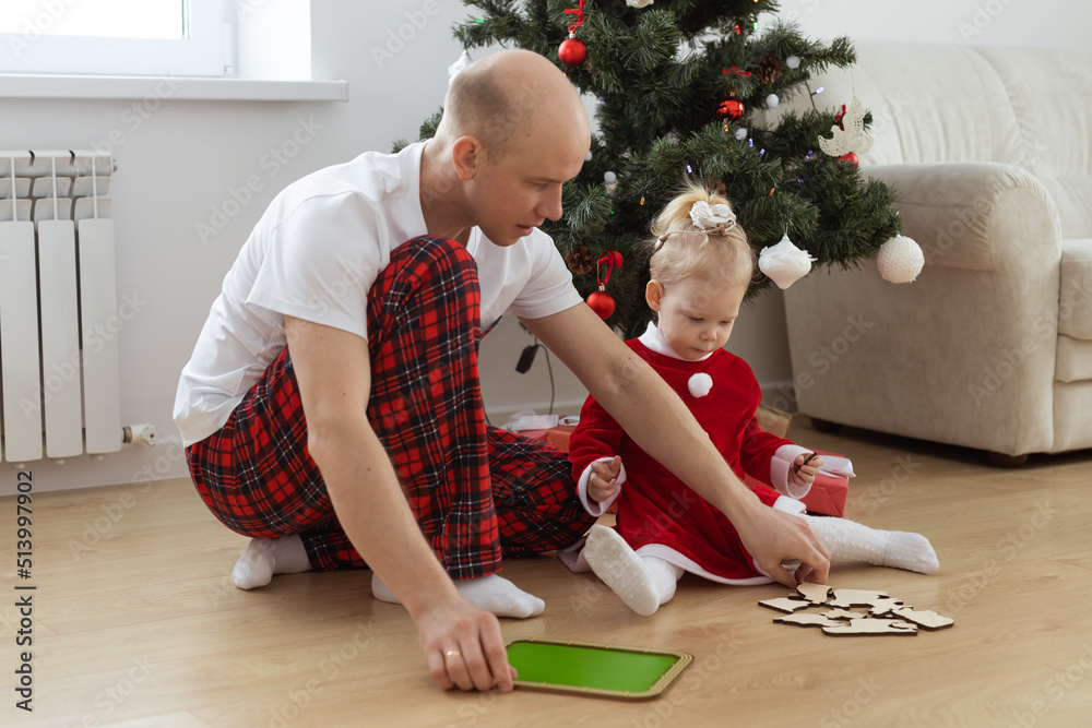 Fototapeta premium Toddler child with cochlear implant plays with father under christmas tree - deafness and innovating medical technologies for hearing aid