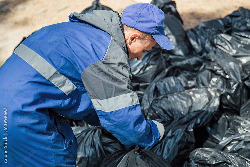Man in overalls ties plastic bags of garbage. Ecological campaign of forest cleaning. Make nature cleaner. Volunteer cleans up garbage. Man in overalls ties plastic bags of garbage. Ecological campaign of forest cleaning. Make nature cleaner. Volunteer cleans up garbage.