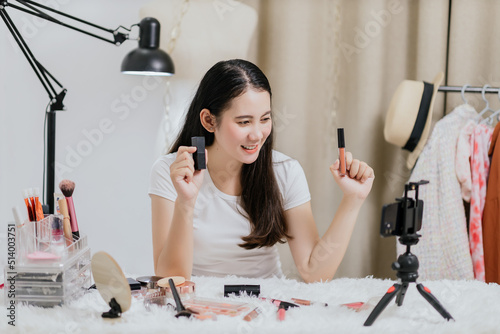 Beautiful Asian woman blogger showing how to make up and use cosmetics live streaming online to social media at home with a smartphone. Beauty blogger or influencer online concept.