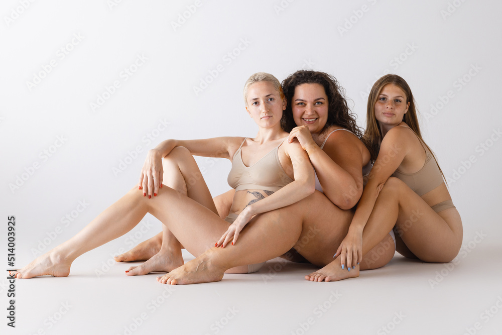Group portrait of beautiful women sitting on floor, posing in underwear isolated over grey studio background Group portrait of beautiful women sitting on floor, posing in underwear isolated over grey studio background