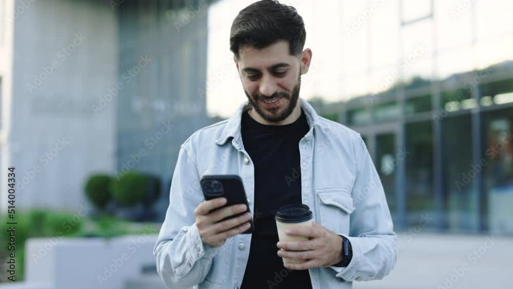 Smiling young attractive bearded man walking use smartphone look around at city center. Handsome man messagen stylish. Employment technology. Slow motion