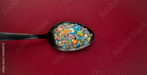 Close-up top shot on micro plastic particles in a spoon against dark red background. Concept for water pollution and global warming.
