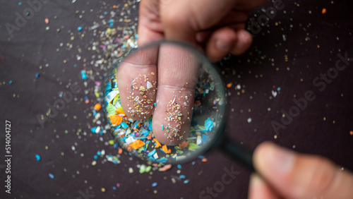 Close-up on micro plastic particles on the fingers under a magnifying glass. Concept for water pollution and global warming. Macro shot on a bunch of microplastics that cannot be recycled