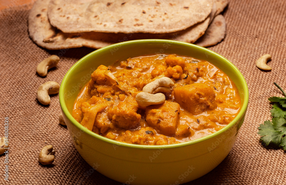 Bowl with indian curry - cauliflower and potato in rich yellow gravy with cashew nuts and flatbread. Aloo gobi on burlap with roti. Bowl with indian curry - cauliflower and potato in rich yellow gravy with cashew nuts and flatbread. Aloo gobi on burlap with roti.