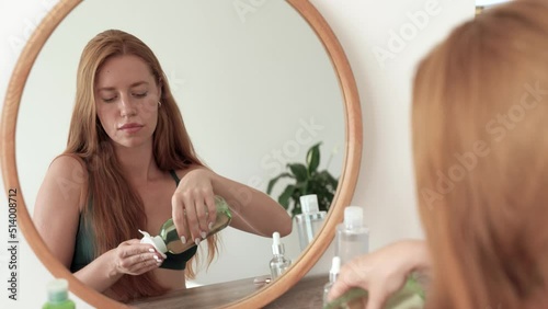 Focused young redhead caucasian woman in mirror reflection applying toner, feeling excited with skin condition Pretty lady using cotton disposable pads, moisturizing skin before starting makeup. 4k