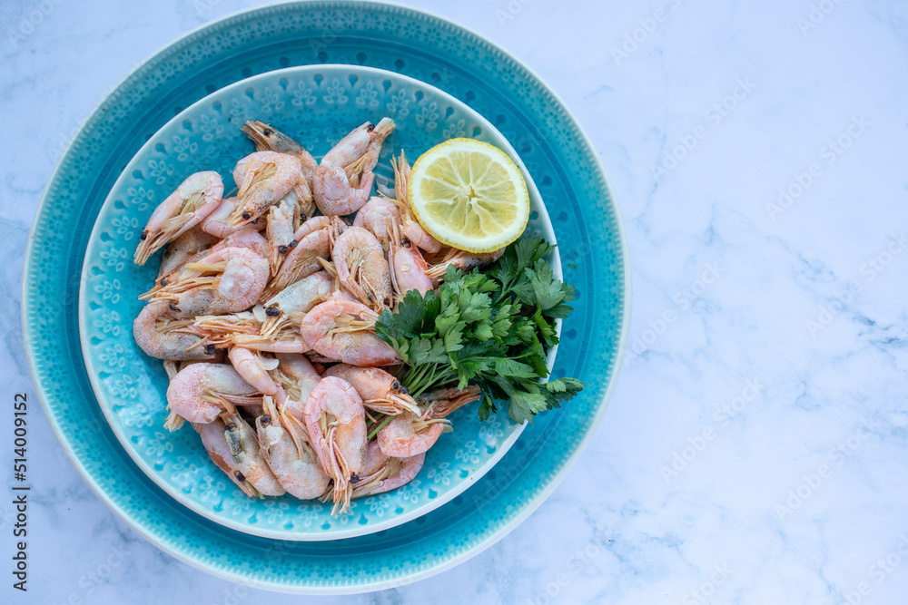 Сooked shrimp with parsley and lemon in a blue ceramic bowl on a white marble table background. Healthy Mediterranean seafood. Top view, flat lay, copy space Сooked shrimp with parsley and lemon in a blue ceramic bowl on a white marble table background. Healthy Mediterranean seafood. Top view, flat lay, copy space