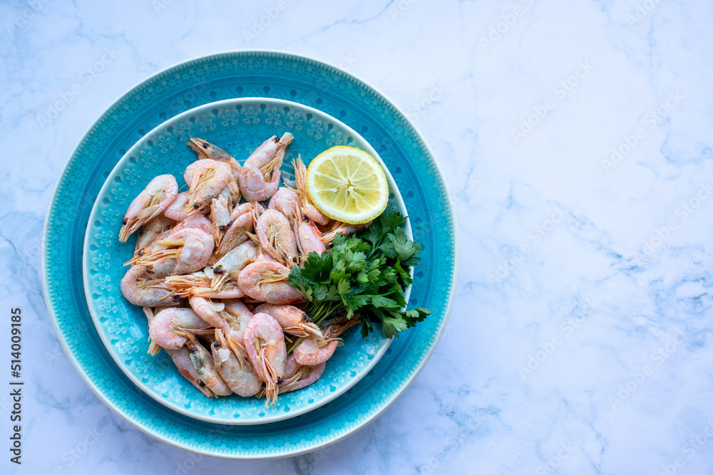 Сooked shrimp with parsley and lemon in a blue ceramic bowl on a white marble table background. Healthy Mediterranean seafood. Top view, flat lay, copy space Сooked shrimp with parsley and lemon in a blue ceramic bowl on a white marble table background. Healthy Mediterranean seafood. Top view, flat lay, copy space