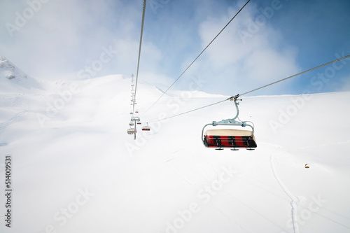An open-air lift that goes to the top of the mountain for downhill skiing. Sunny day surrounded by snowy fields. Ski resort slope in good weather