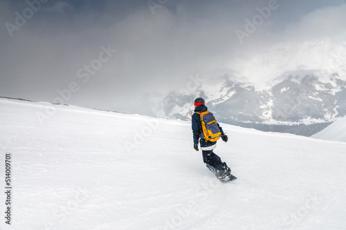 Young sportswoman snowboarder ride on a snowy slope against the backdrop of mountains on a winter day at a ski resort