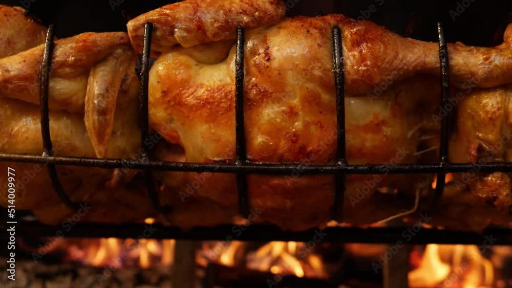 Slow motion closeup of a Roasted chickens on spit grilled over wood fire on big bbq barbecue 