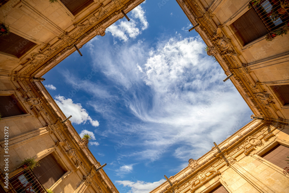 Interior of the arcaded baroque cloister of the Episcopal Palace in Murcia, Spain, from an original perspective in which the sky with clouds is seen