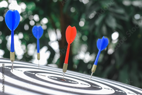 Red dart arrow hit the center target of dartboard and blue dart arrow hit out of center with blur background. Target business or market goals concept