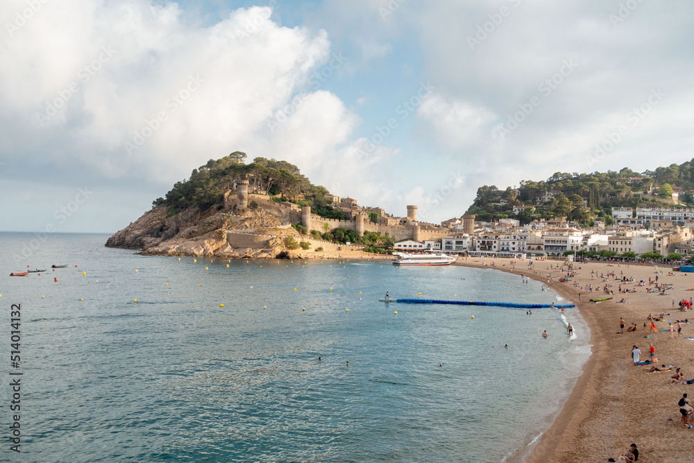 view of the beach and the castle of tossa de mar in a summer day with clouds, catalonia, spain