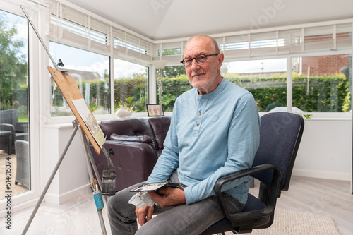 Environmental  portrait of  a senior artist painting with watercolours in his home studio.