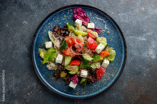 Greek salad with feta cheese and vegetables on blue plate on dark grey table top view