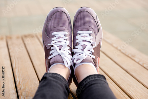 Womens legs in pink sneakers. Womens sports shoes on wooden planks. Side view