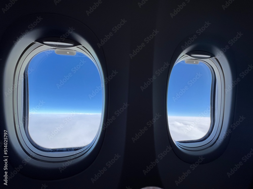 Looking through silhouetted airplane windows at white, fluffy clouds below and deep indigo sky overhead Looking through silhouetted airplane windows at white, fluffy clouds below and deep indigo sky overhead