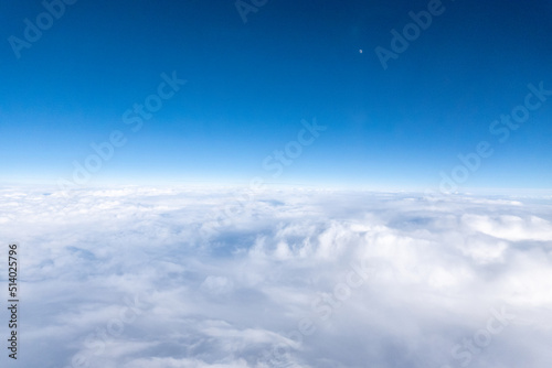 View from airplane window of white, fluffy clouds below and deep indigo sky overhead