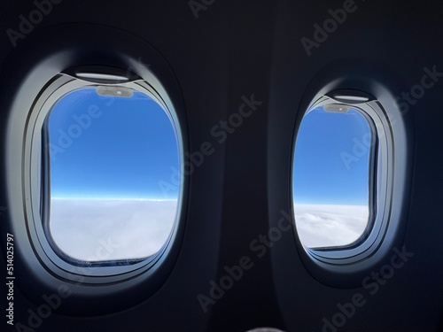 Looking through silhouetted airplane windows at white, fluffy clouds below and deep indigo sky overhead