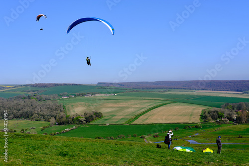 Eastbourne, UK. 16 April 2022. Paragliding concept, group of paragliders flying in countryside against clear blue sky. Low angle view.