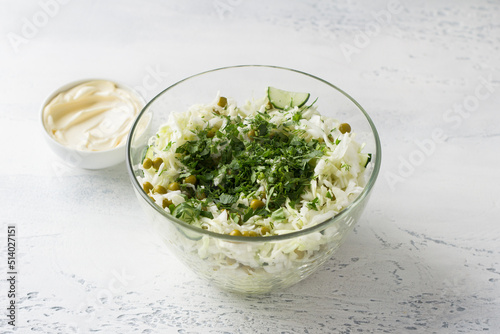 Glass bowl of cabbage salad with cucumbers, green peas, chopped herbs and mayonnaise dressing. Cooking delicious homemade salad. Step-by-step instruction. Step 3