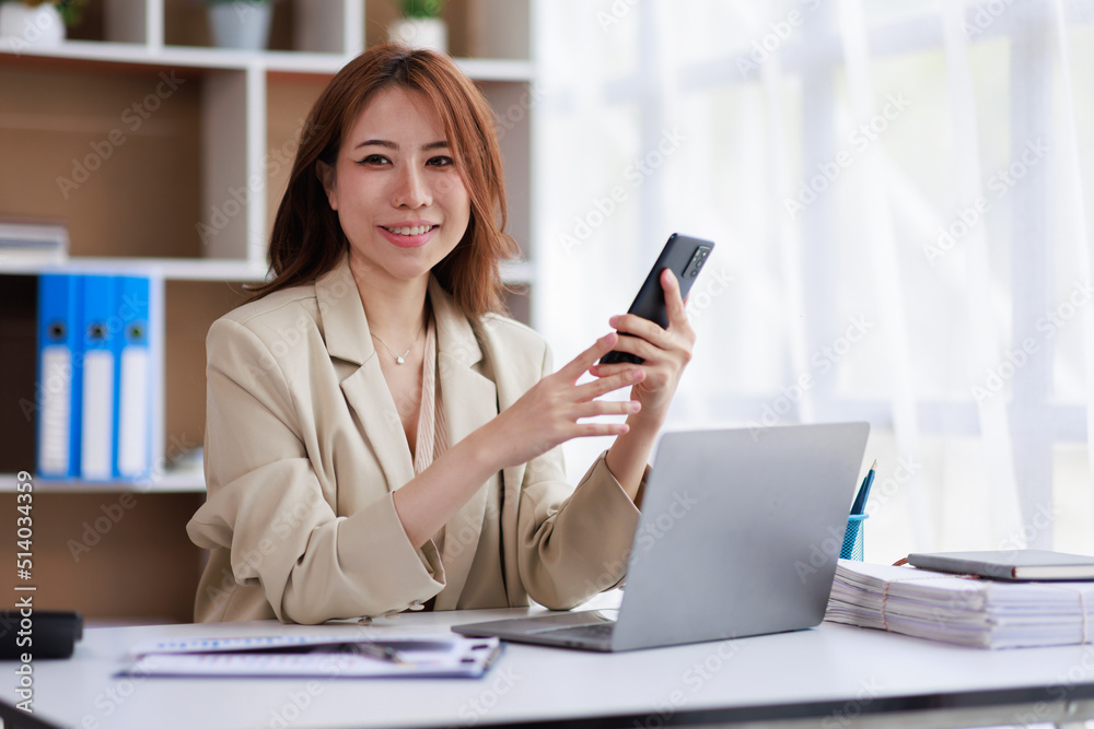 Asian Businesswoman uses a mobile phone and works on laptop computer in the modern home office. Asian Businesswoman uses a mobile phone and works on laptop computer in the modern home office.