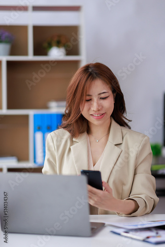 Asian Businesswoman uses a mobile phone and works on laptop computer in the modern home office.