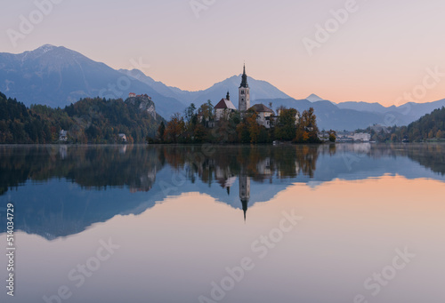 Lake Bled at Sunrise. Church, castle and the mountains are basking in the morning sun