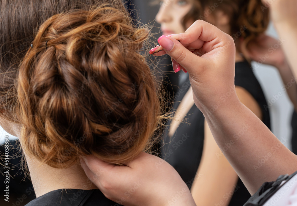 The hairdresser makes a hairstyle to a young attractive woman with a beautiful make-up in a black dress in a beauty salon. The hairdresser makes a hairstyle to a young attractive woman with a beautiful make-up in a black dress in a beauty salon.