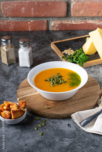 Dietary vegetarian pupmkin cream soup puree, on dark brown wooden table, side view, close up. Vertical photo