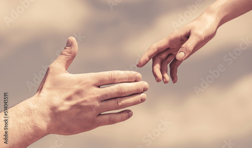 Giving a helping hand. Hands of man and woman on blue sky background. Lending a helping hand. Hands of man and woman reaching to each other, support. Solidarity, compassion, and charity, rescue