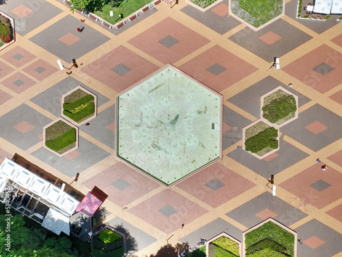 Park with arranged cobblestones in the shape of rhomboids. A fountain in the shape of an octagon. Green trees. South Park. View from above.