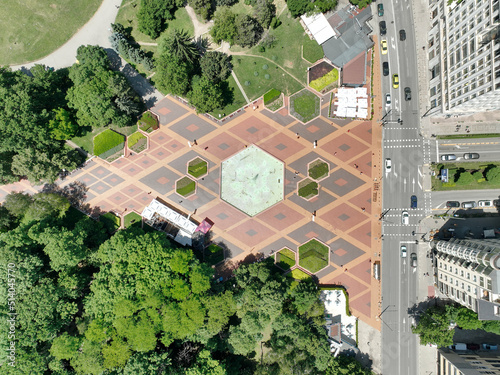 Park with arranged cobblestones in the shape of rhomboids. A fountain in the shape of an octagon. Green trees. South Park. View from above.