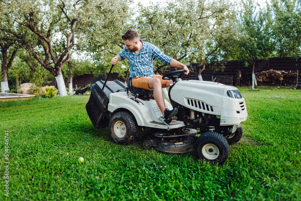 Fototapeta premium Gardener worker using lawn tractor and cutting grass through garden