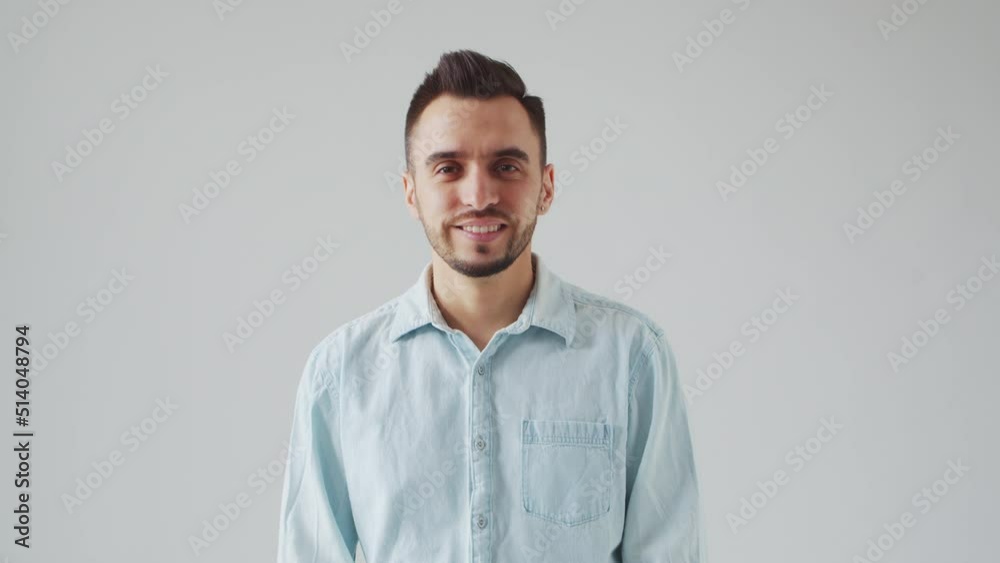 Young Caucasian Brunet Man is Looking at the Camera on a Light Gray Background. Studio Male Face Portrait. Natural Day Light. Young Caucasian Brunet Man is Looking at the Camera on a Light Gray Background. Studio Male Face Portrait. Natural Day Light.