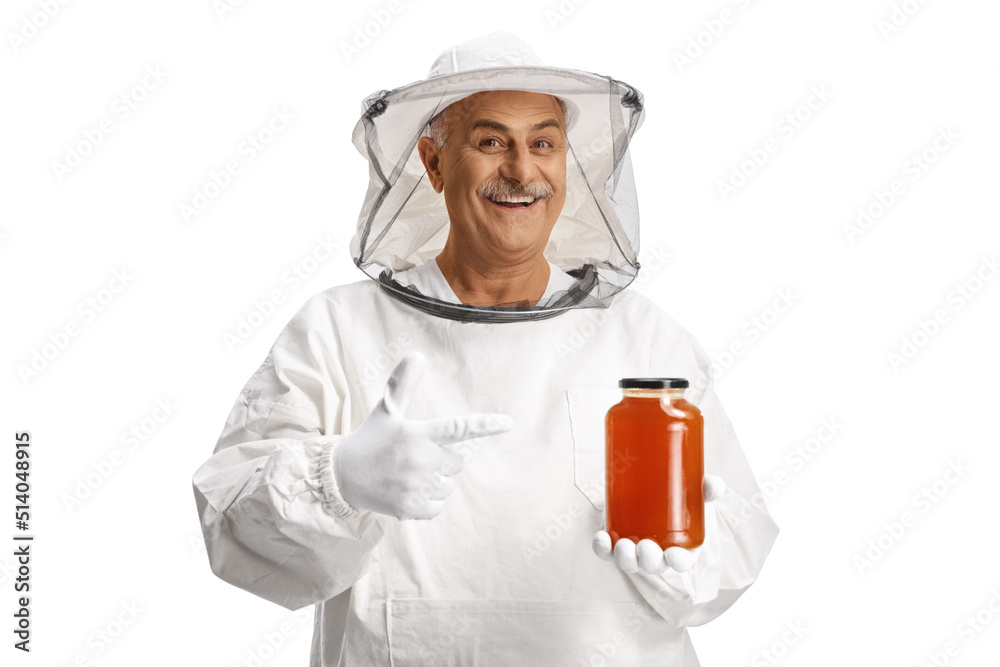 Mature male bee keeper in a uniform holding a jar of honey and pointing Mature male bee keeper in a uniform holding a jar of honey and pointing