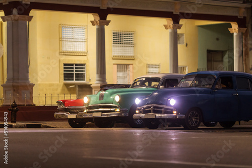 Amazing old american car on streets of Havana with colourful buildings in background during the night. Havana, Cuba.