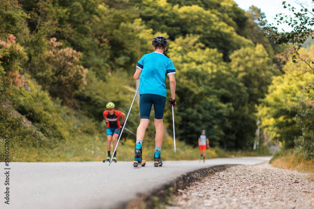 Group of sportsmen training before the competition. View from the back. Biathlon ride on the roller skis with ski poles, in the helmet. Concept of sport and summer contest Group of sportsmen training before the competition. View from the back. Biathlon ride on the roller skis with ski poles, in the helmet. Concept of sport and summer contest